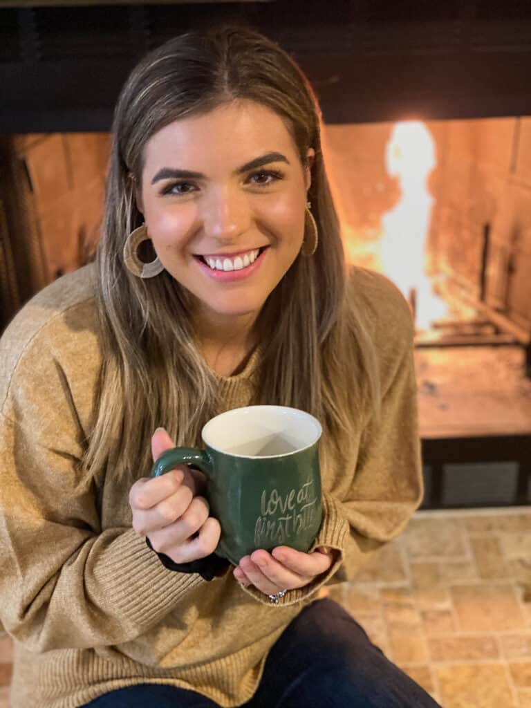 This is a photo of Bri by the fire with her mug that says "love at first bite".