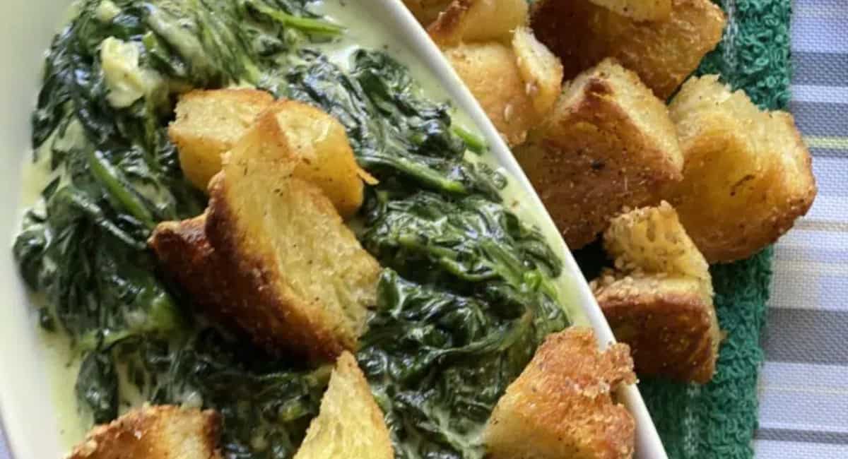 Creamed spinach topped with croutons on a white serving dish.