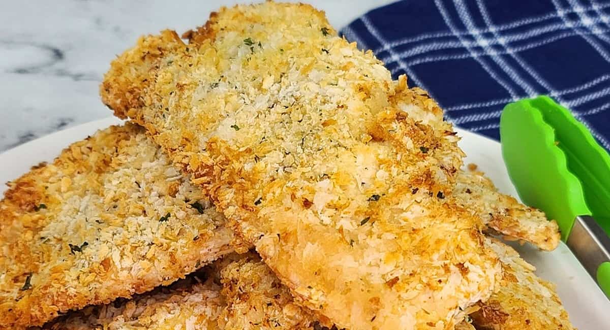 Chicken cutlets served on a white plate and next to green tongs.