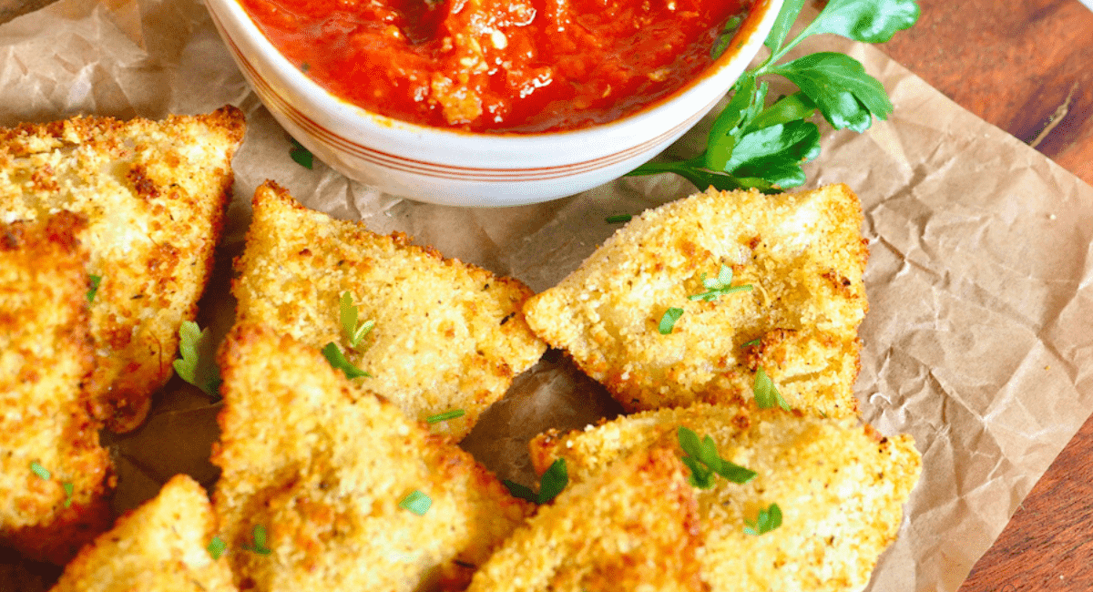 Fresh air fried ravioli served with a marinara sauce on a wood board.