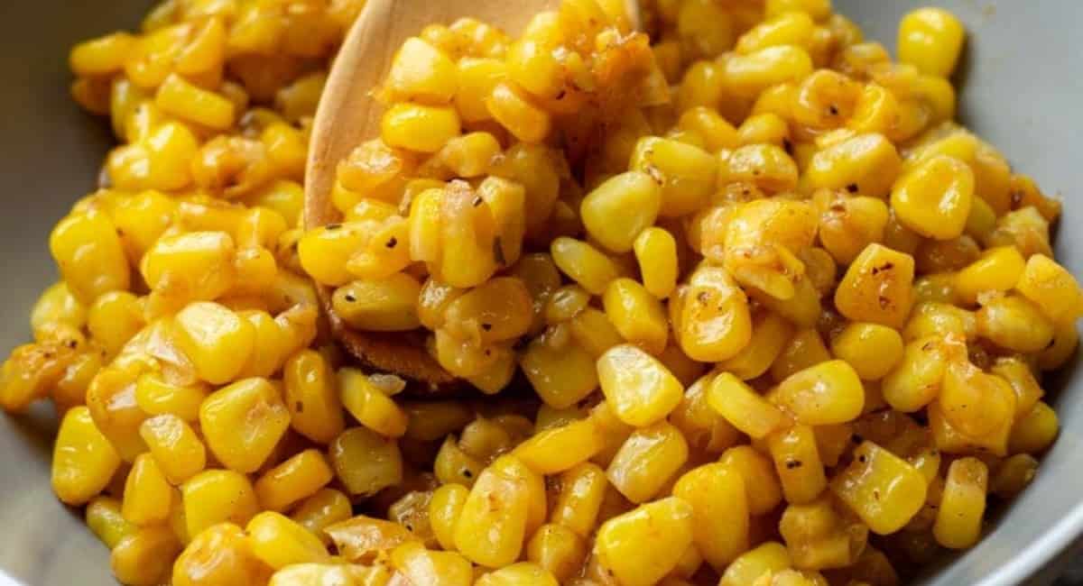 Cajun corn in a white bowl and being scooped with a wooden spoon.