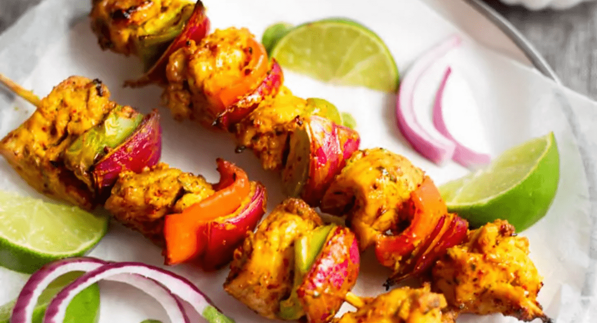 Chicken tikka kebabs served on a white plate with sliced onion and limes.