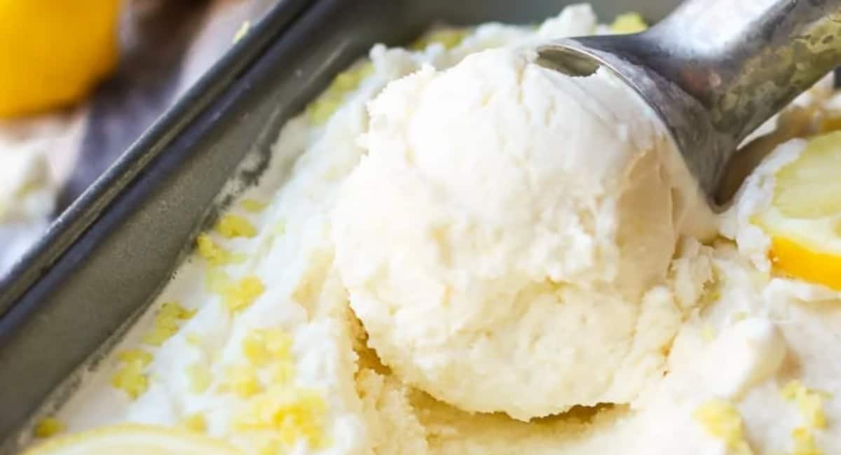 Lemon ice cream in a tray and being scooped out with an ice cream scooper.