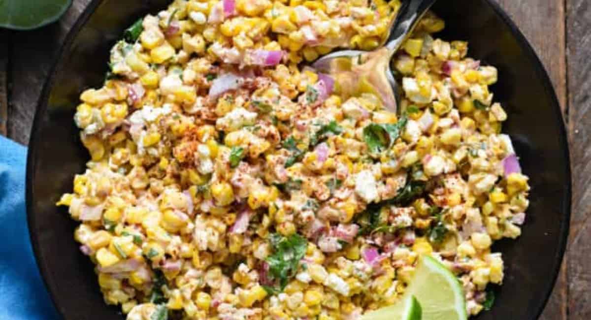 Corn salad topped with onions and limes in a black bowl.