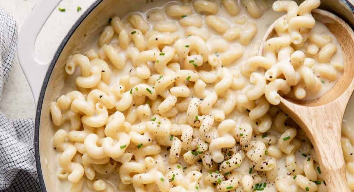 Mac and cheese in a white dutch oven and being scooped with a wooden spoon.