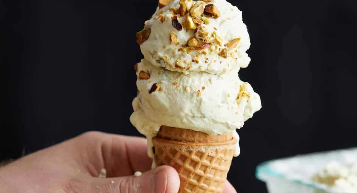 Double scoop of pistachio ice cream on a cone with nuts on top.