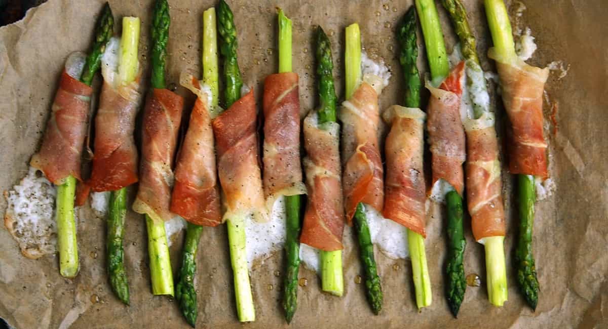 Bacon and goat wrapped asparagus on a wood board.