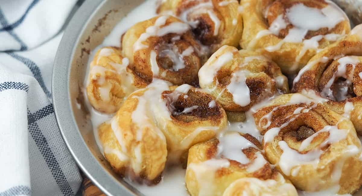 Air fryer cinnamon rolls served in a pie pan and topped with cream cheese icing.