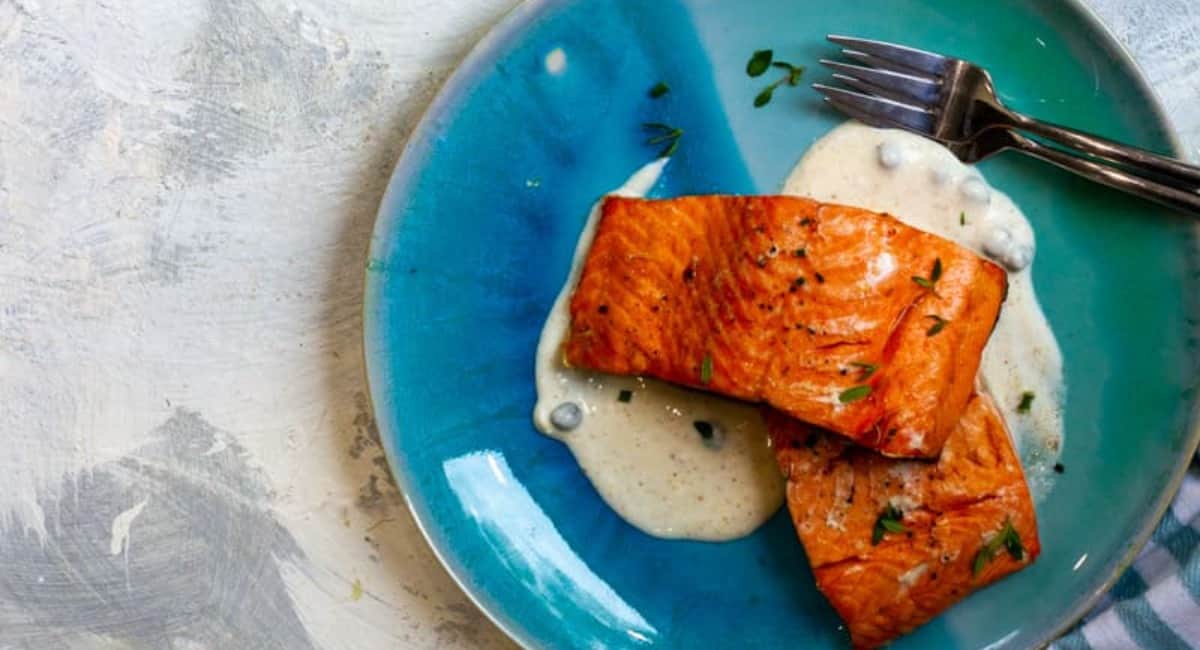 Salmon fillets served over a homemade cream sauce on a blue plate.