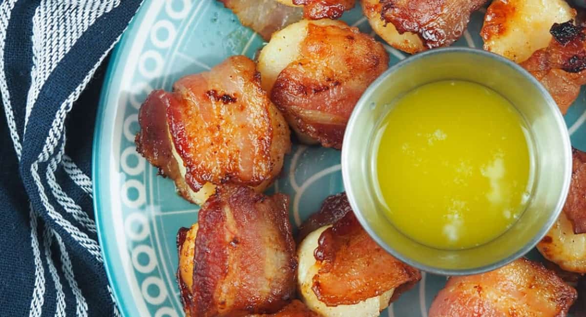 Bacon wrapped scallops on a blue plate, with a homemade dipping sauce.