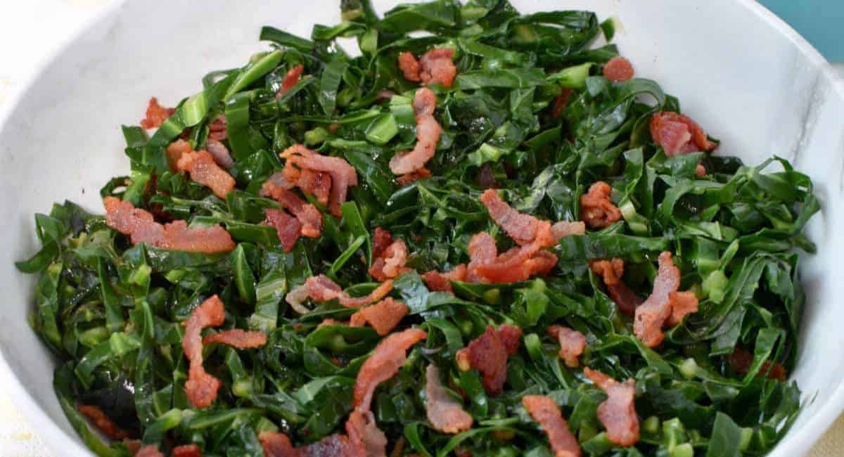 Collard greens topped with bacon and in a white bowl.