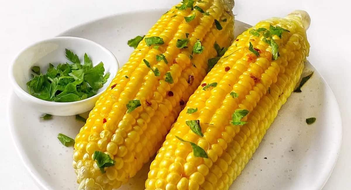 Grilled corn on the cob topped with parsley and served on a white plate.