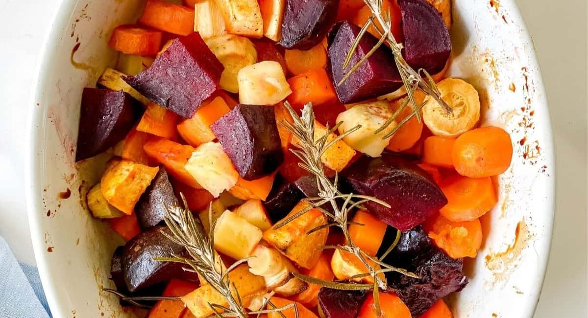 Honey roasted vegetables topped with rosemary in a white casserole dish.