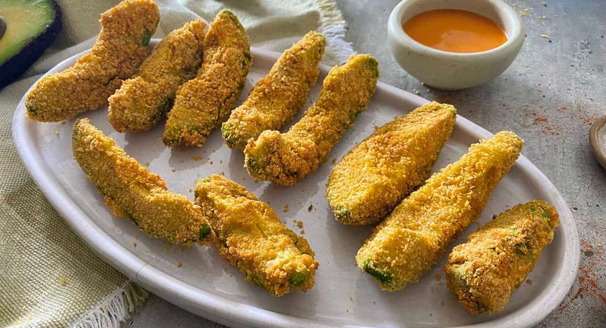 Fried avocado fries served on a white plate with a homemade dipping sauce.