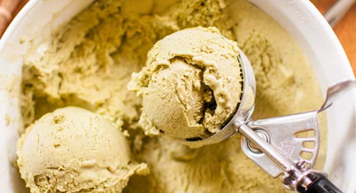 Green matcha ice cream in a white bowl being scooped by an ice cream scooper.