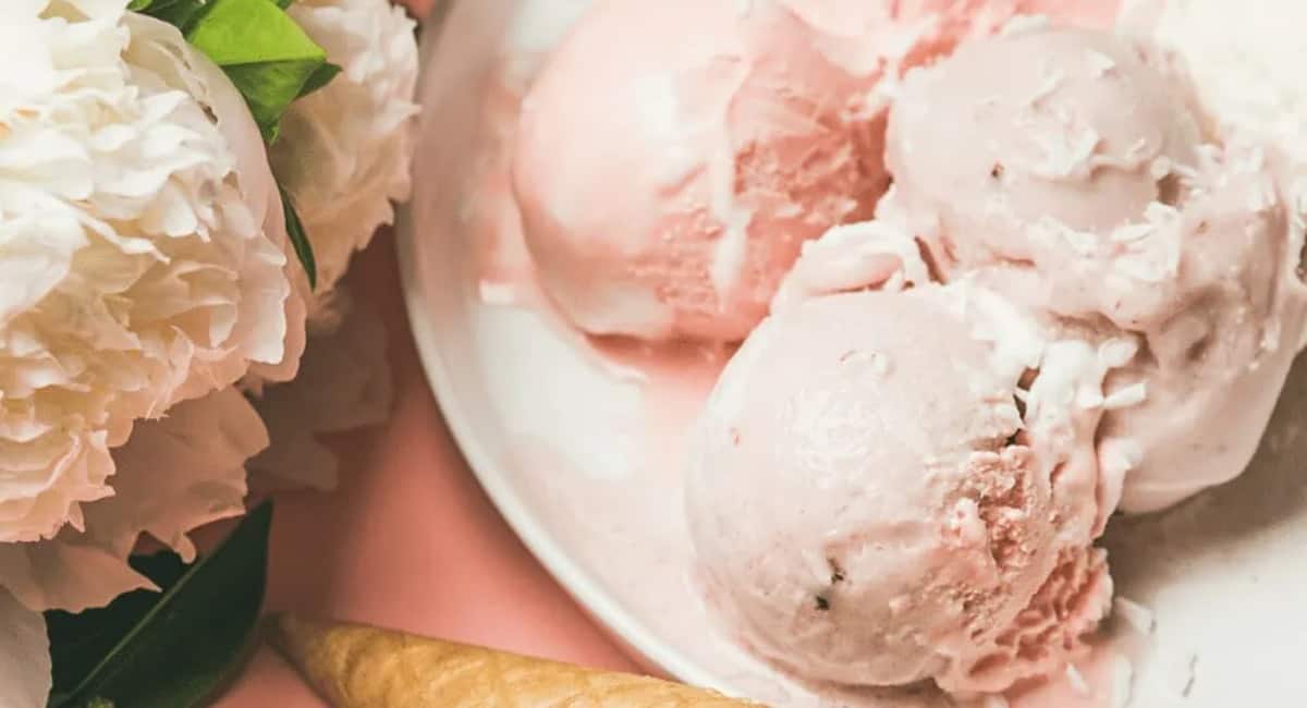 Strawberry vanilla ice cream served on a white plate next to flowers.