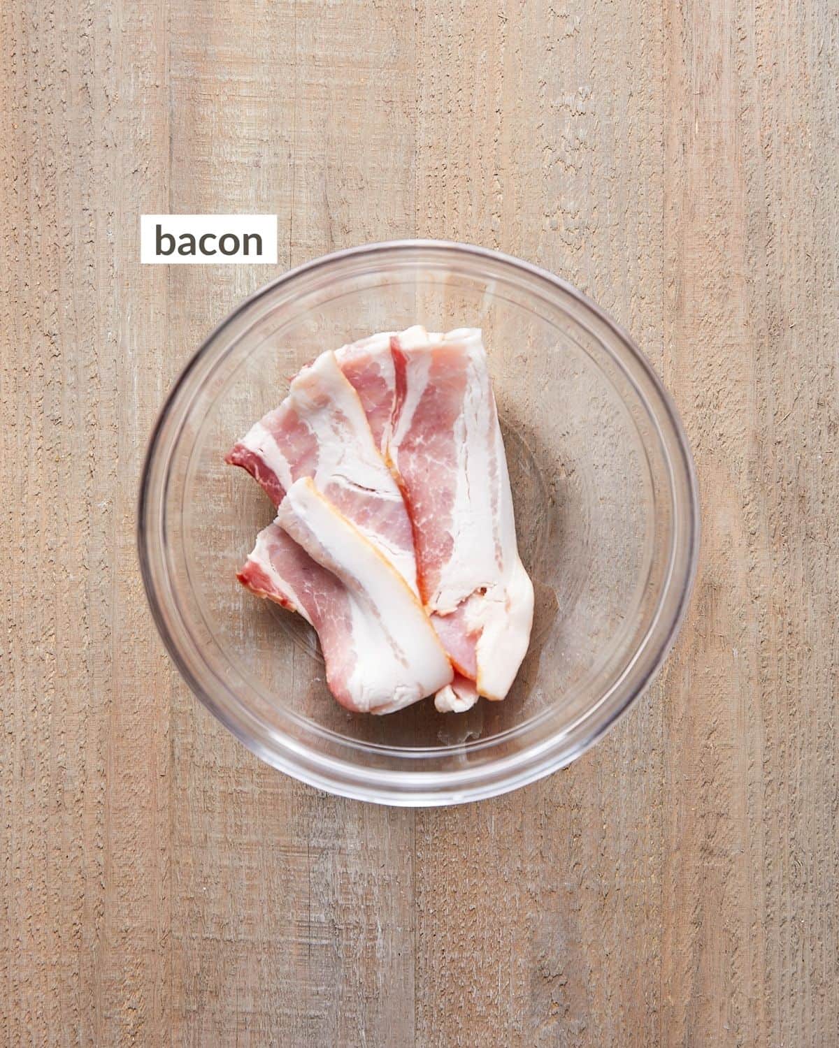 Overhead of raw bacon strips in a bowl.