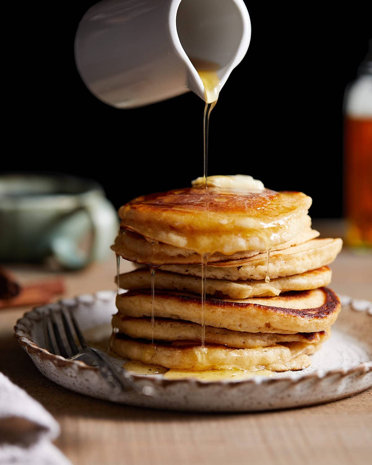 Stack of fluffy pancakes on white plate with maple syrup. 