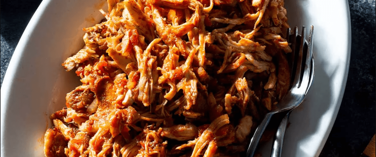 Oven pulled chicken thighs in white dish with fork. 