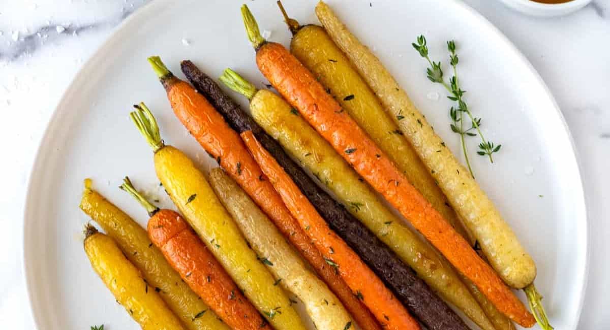 Photo of honey thyme roasted rainbow carrots on white dish.