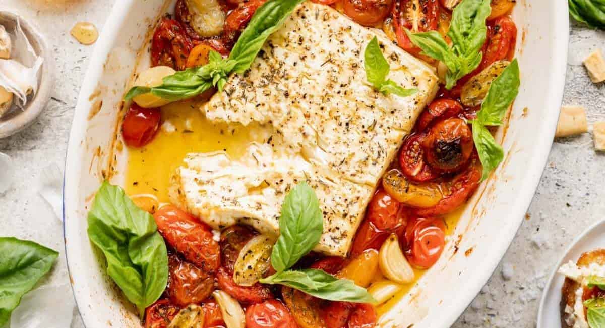 Overhead image of baked feta with tomatoes in white dish with garnish.