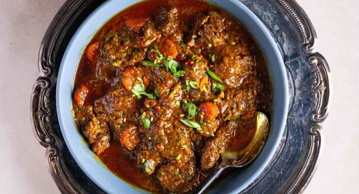 Overhead image of beef masala in blue dish with garnish.