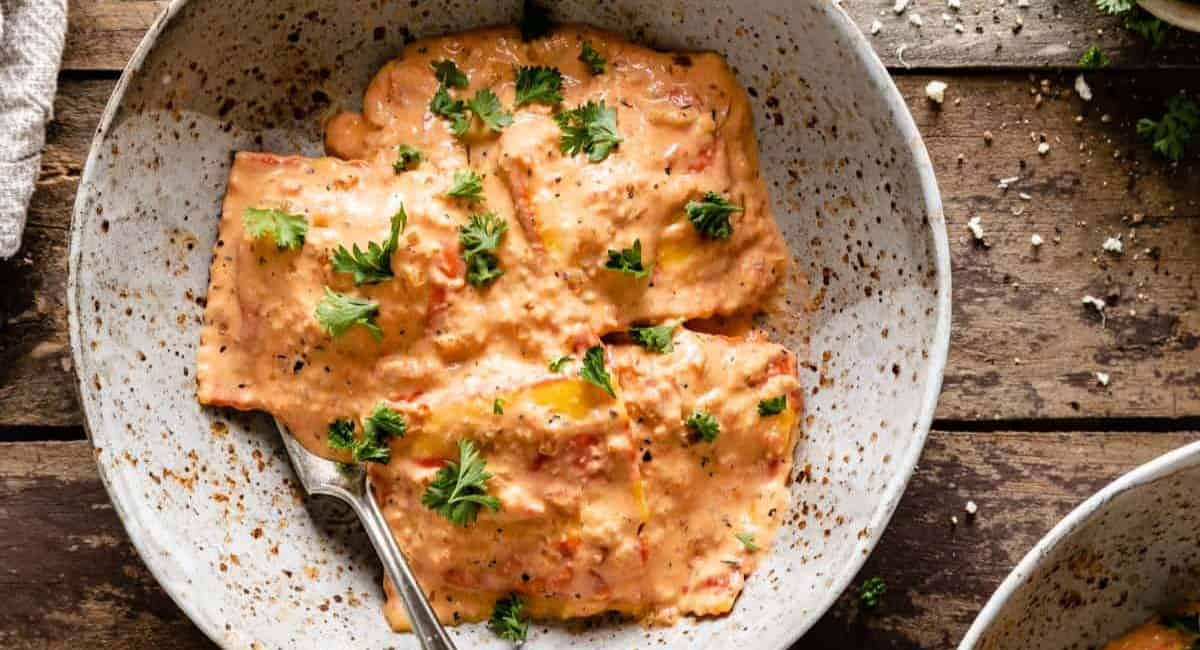 Overhead image of lobster ravioli sauce in white dish with garnish.