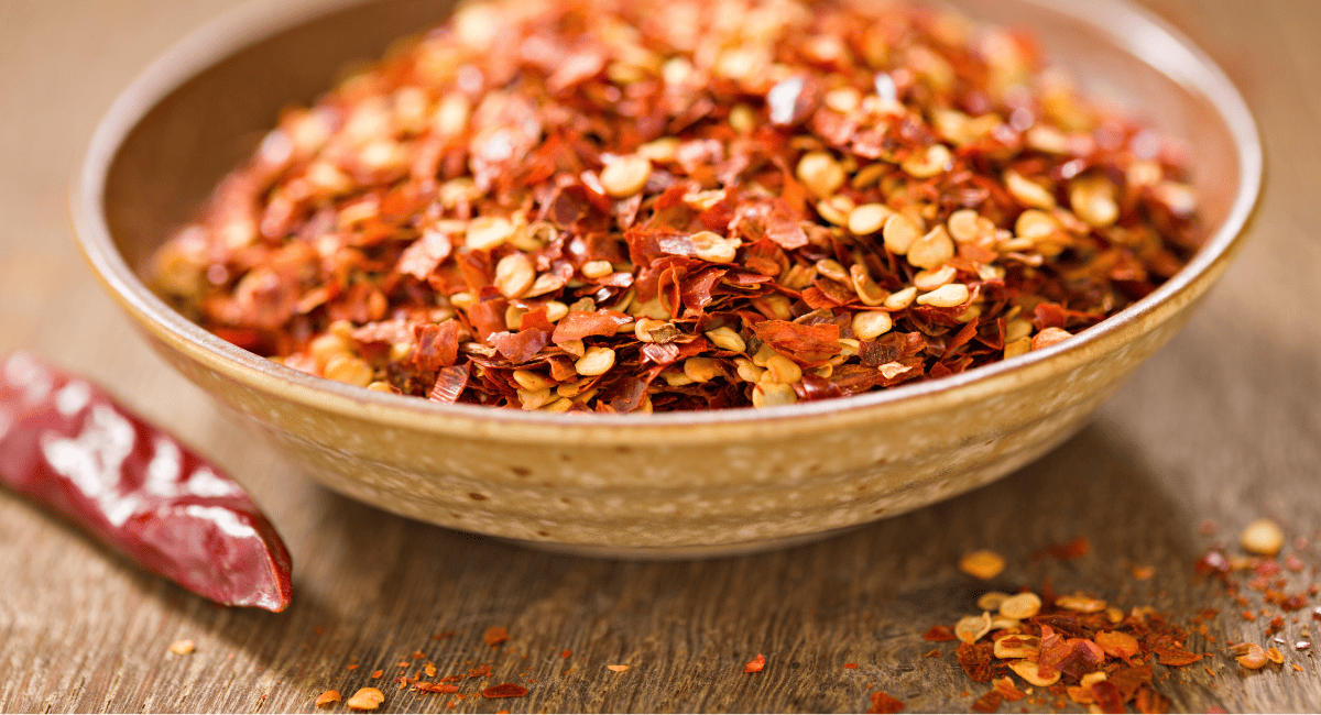 Up close image of red pepper flakes in brown bowl.