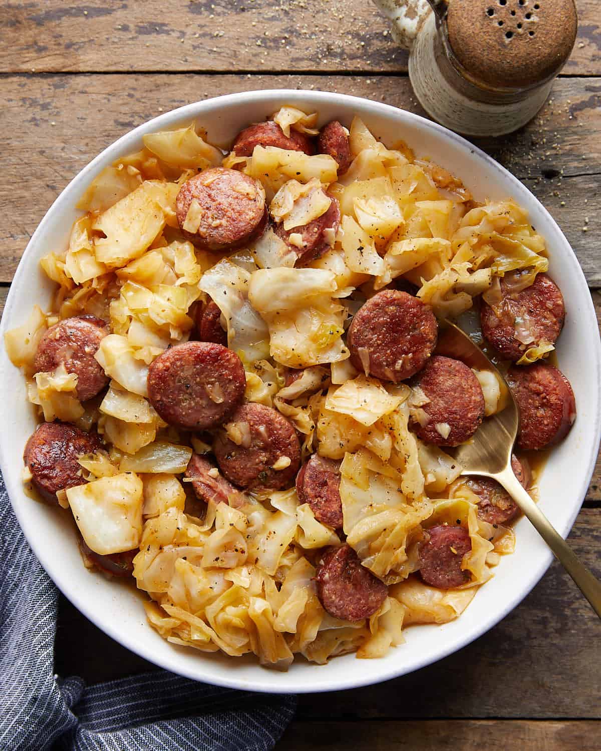 Overhead image of smoked sausage and cabbage in white dish.