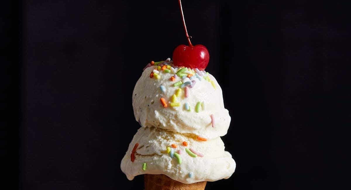 Up close image of no egg vanilla ice cream with sprinkles and a cherry on top. 