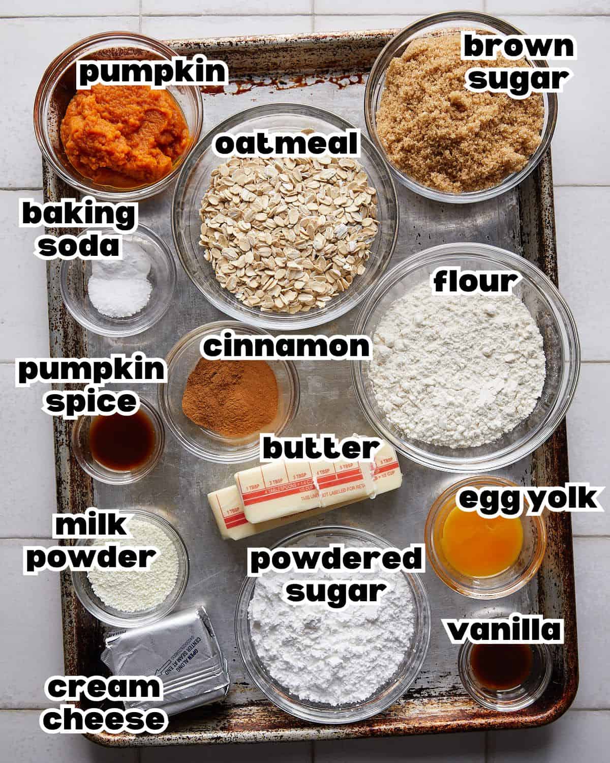 Overhead image of ingredients needed to make pumpkin oatmeal cookies, including pumpkin puree, oats, flour, sugar, spices, and butter arranged in bowls.