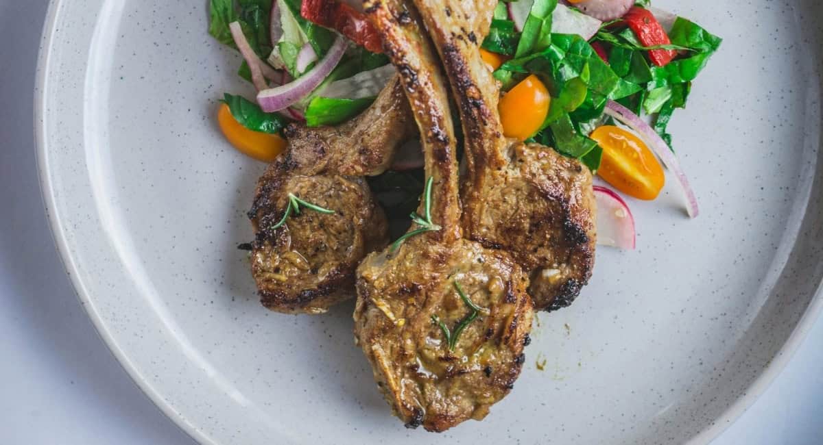 Overhead image of lamb chops with roasted garlic marinade and salad side dish. 