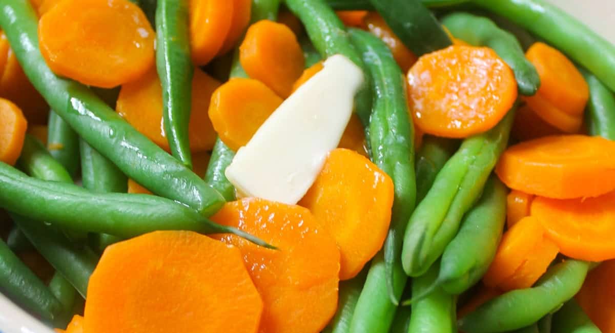 Up close image of siple green beans and carrots with butter. 