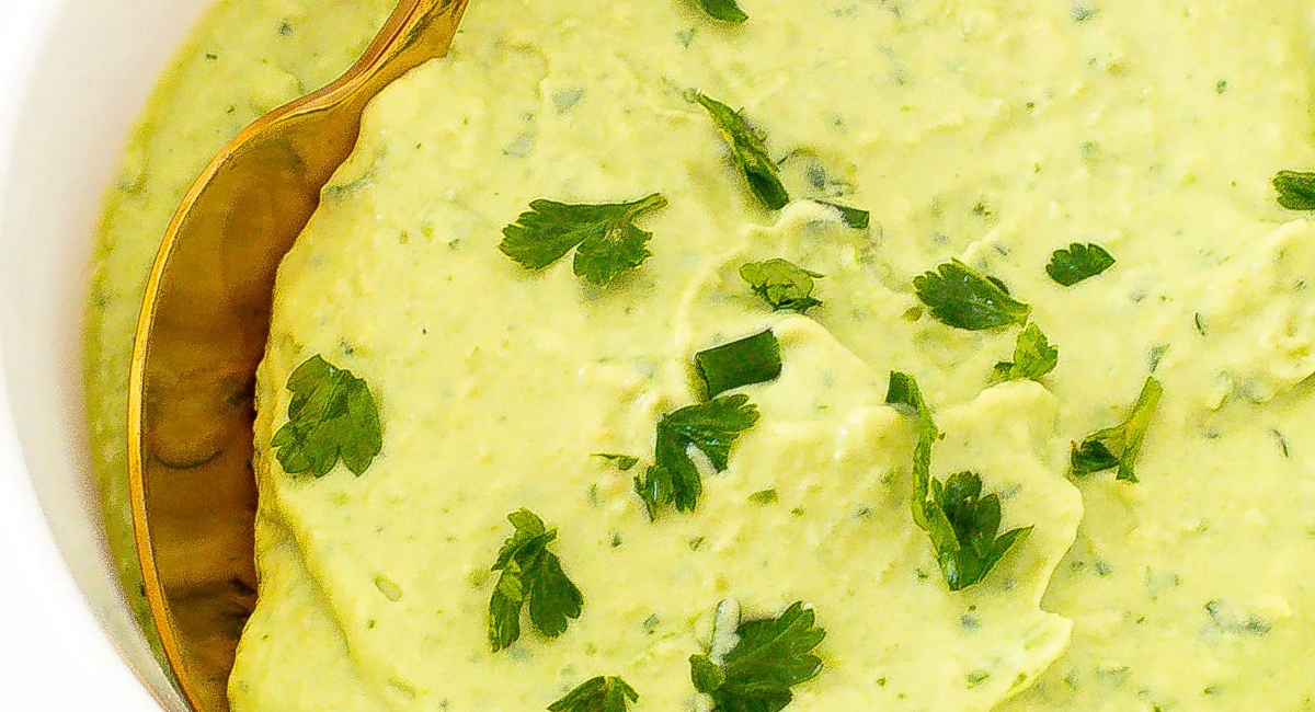 Overhead image of avocado crema with garnish in white dish with spoon dipped in. 