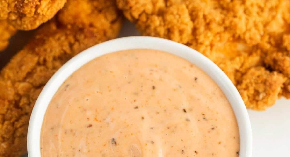 Overhead image of chicken dipping sauce with chicken trips in the background. 