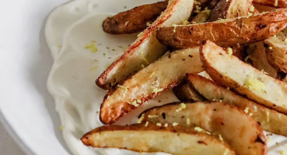 Up close image of air fryer potato wedges on a whipped feta dip. 