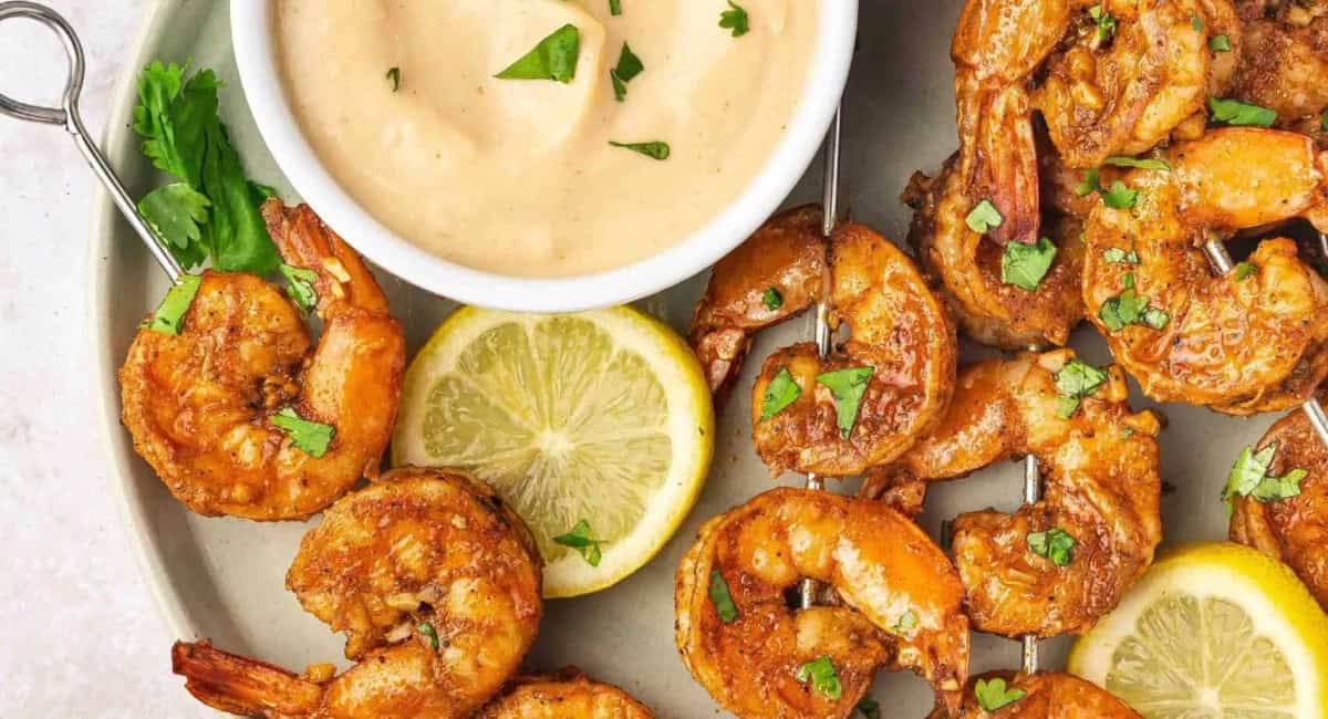 Overhead image of oven shrimp skewers with garnish and sauce. 