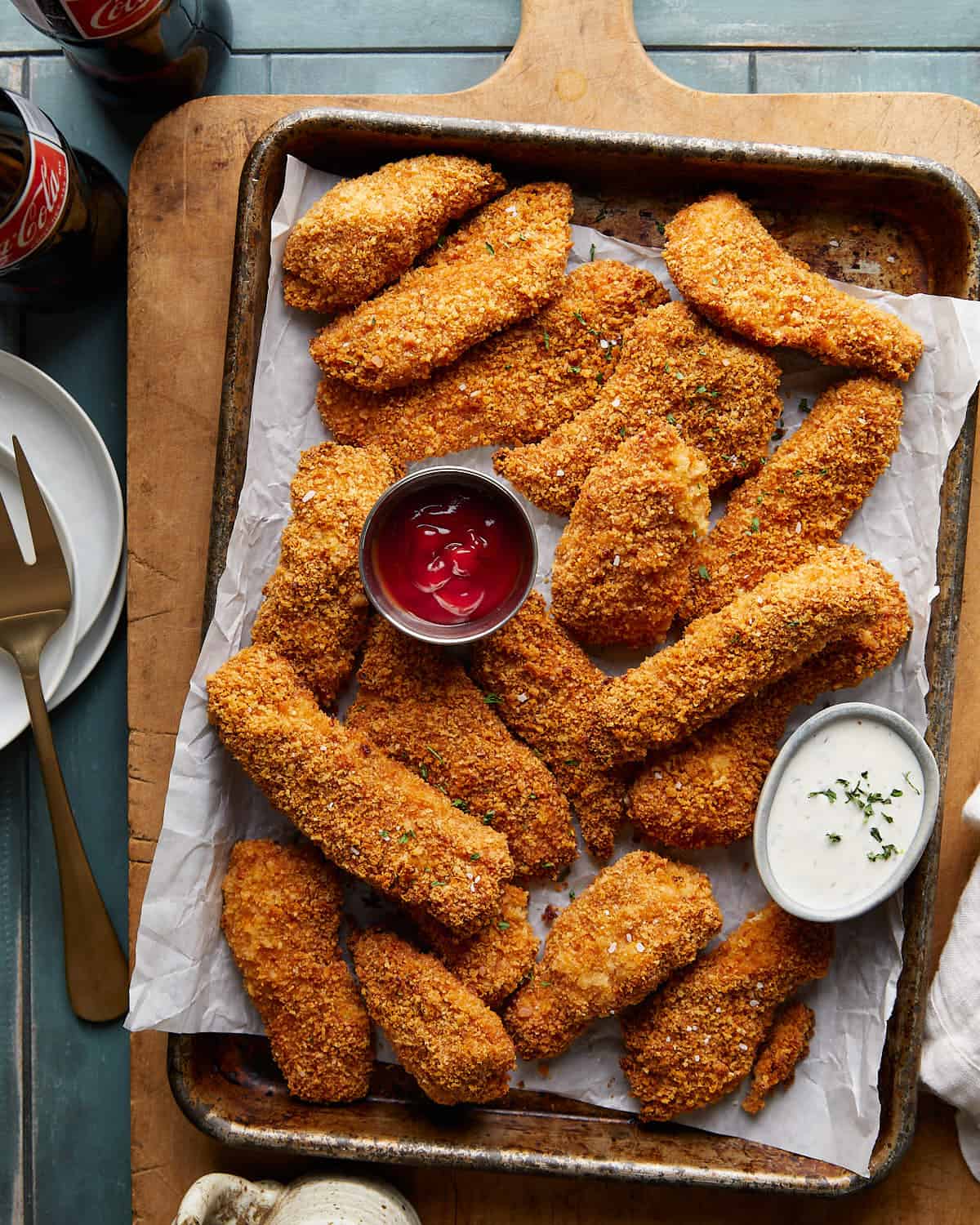 Overhead image of crispy chicken tenders with ketchup and ranch dips on baking sheet.