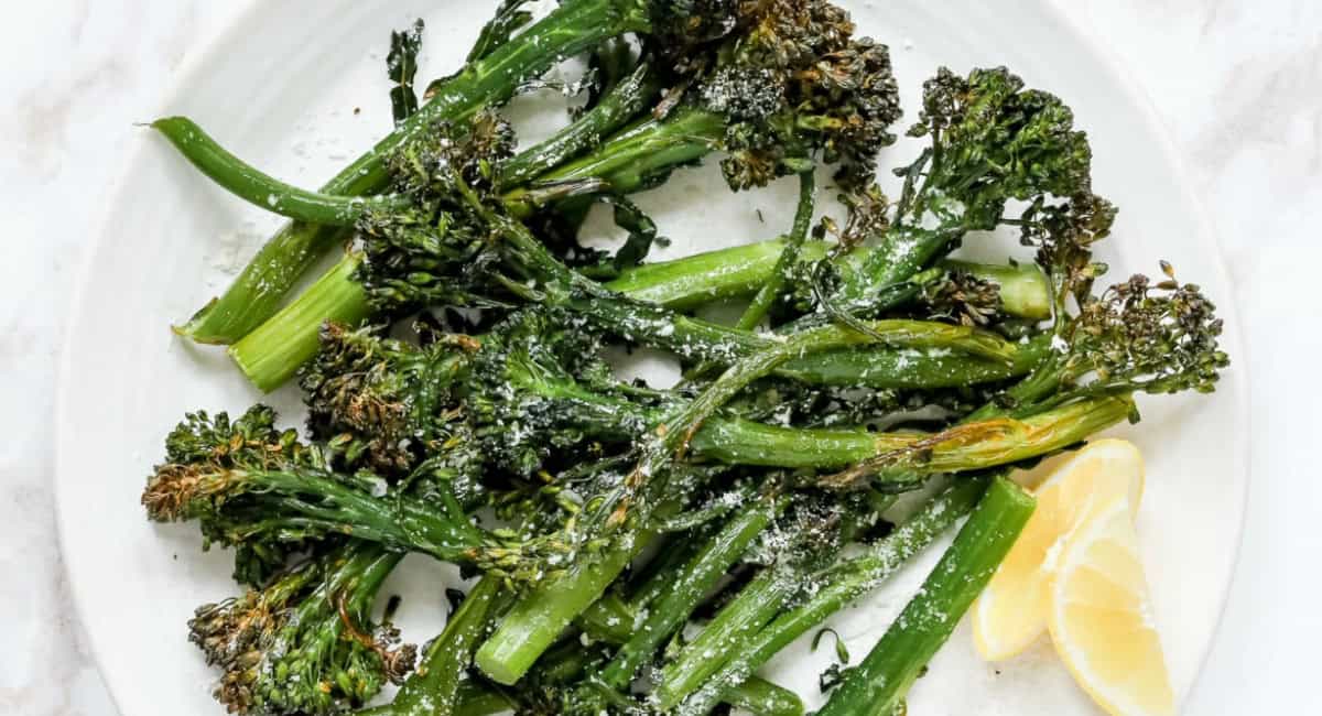Overhead image of air fryer broccolini with lemon wedge. 