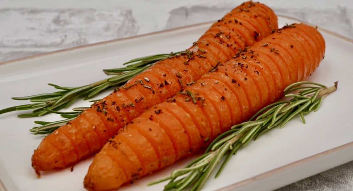 Up close overhead image of hasselback carrots with honey and rosemary on white dish. 