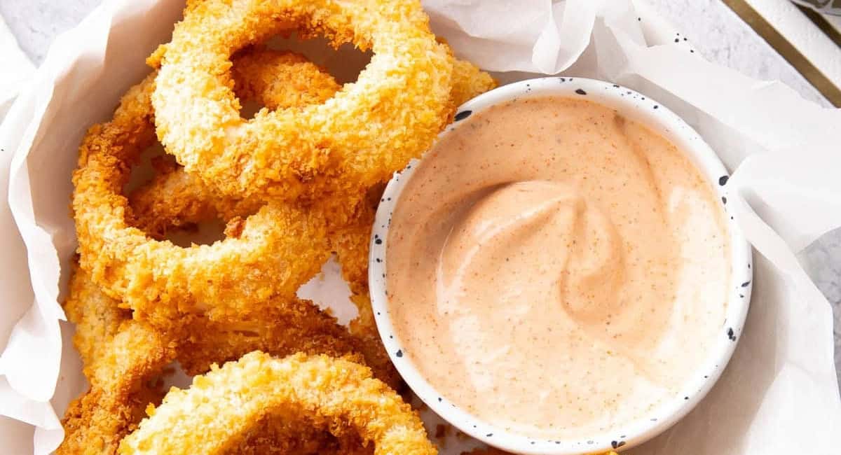 Overhead image of air fryer onion rings with sauce in small bowl on the side. 