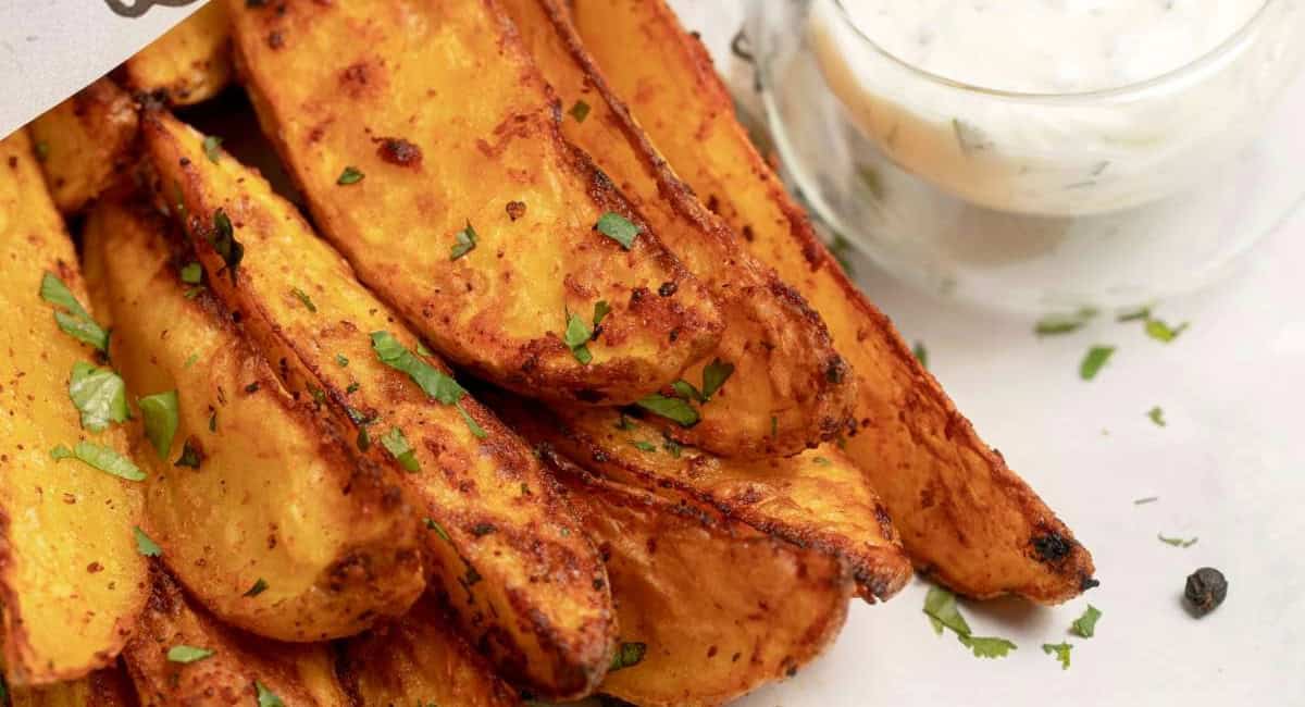 Overhead image of air fried potato wedges with garnish. 