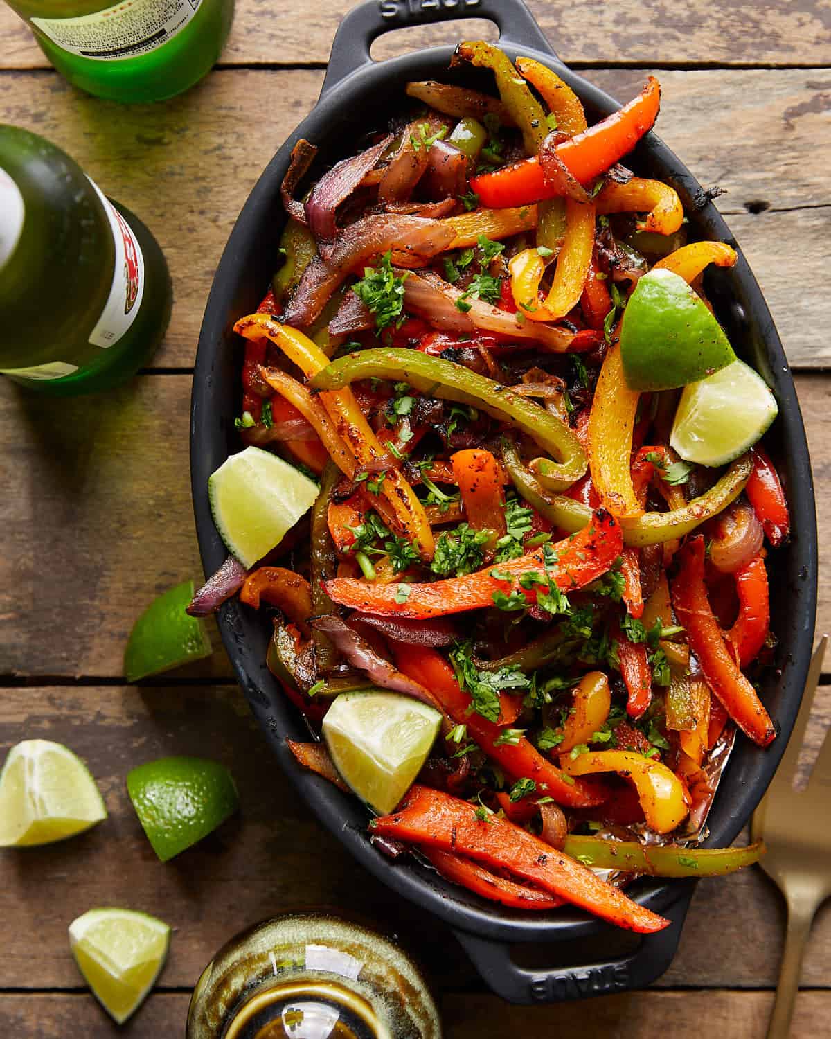 Overhead image of grilled peppers and onions in black dish with garnish.