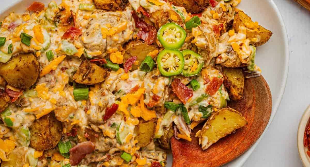 Overhead image of jalapeno popper potato salad on white dish with wooden spoon. 