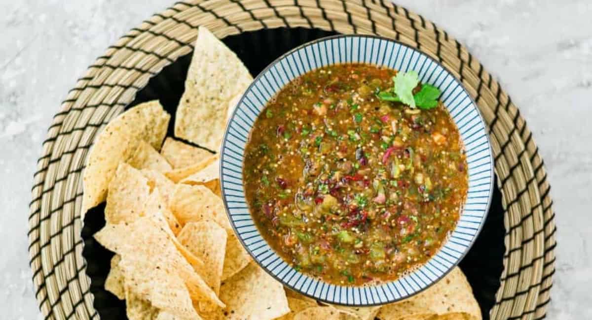 Overhead image of tomatillo-chipotle salsa with garnish and nacho chips. 