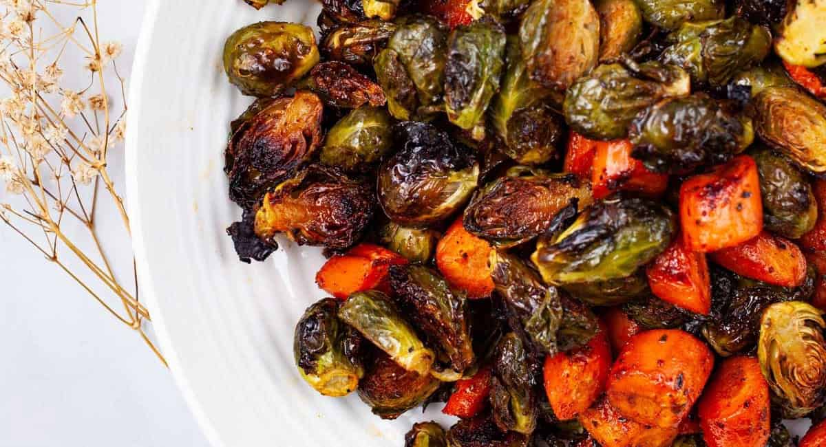 Overhead image of sweet and spiced roasted brussels sprouts and carrots in white dish. 