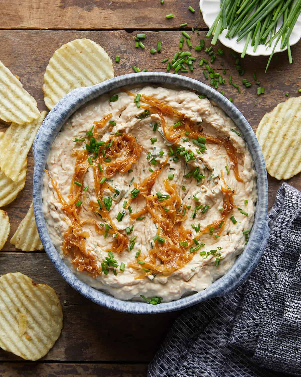 Overhead image of homemade caramelized french onion dip with garnish and potato chips.
