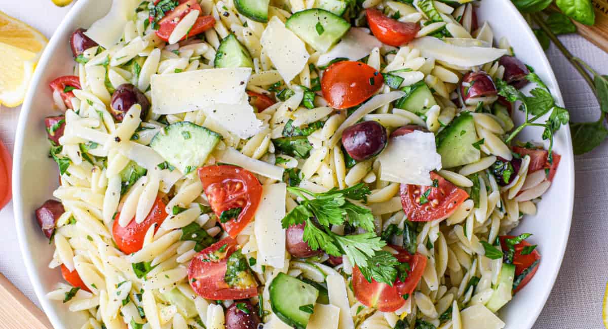 Overhead image of lemon orzo salad with garnish in white bowl. 