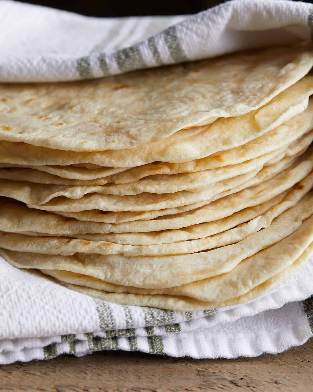 Up close side image of homemade flour tortillas wrappted around striped towel. 