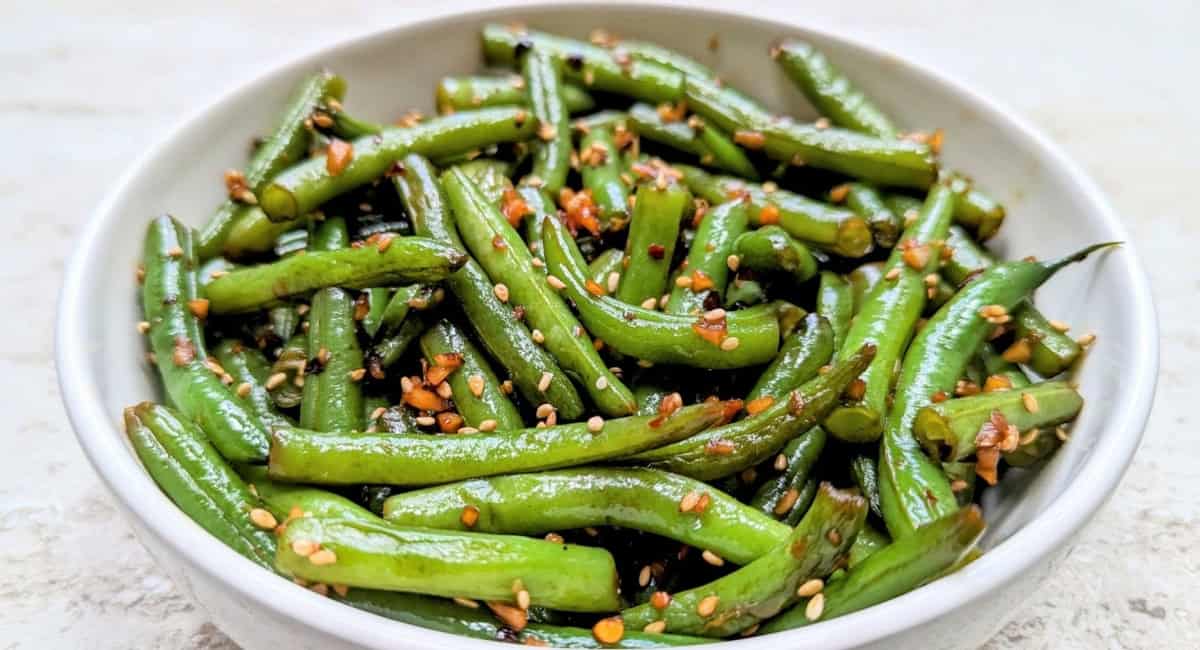 Overhead image of garlic sesame green beans with garnish in white bowl. 